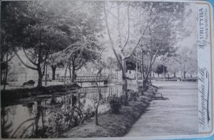 Curitiba - Postal em preto e branco que destaca um dos canais artificiais do Rio Belém, no início do século XX. Ao fundo da imagem, vê-se uma ponte. Postal da Coleção e Acervo de Paulo Affonso Grötzner.